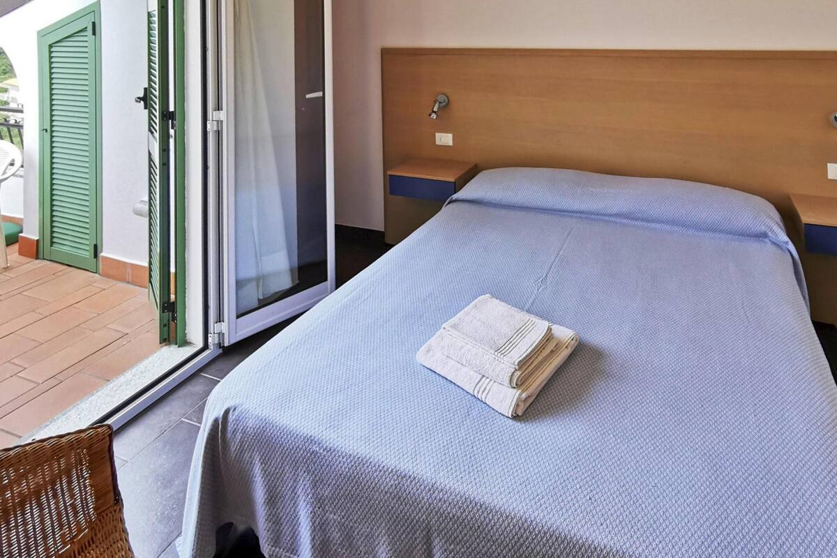 A hotel room with a bed, a nightstand, a green door, and a sliding glass door leading to an outdoor area.