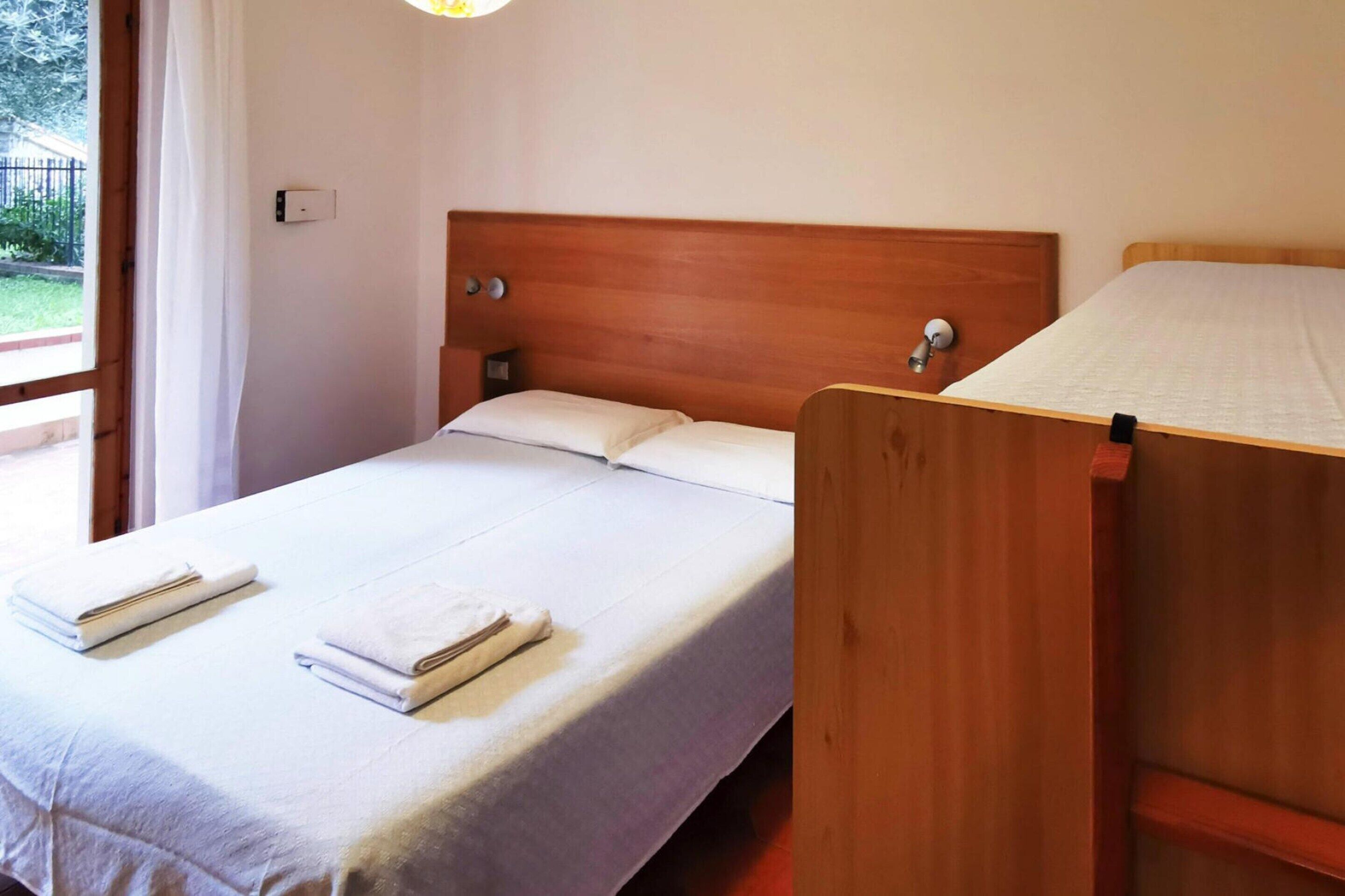 A single bed with a wooden headboard, a bedside table, and two neatly folded towels.