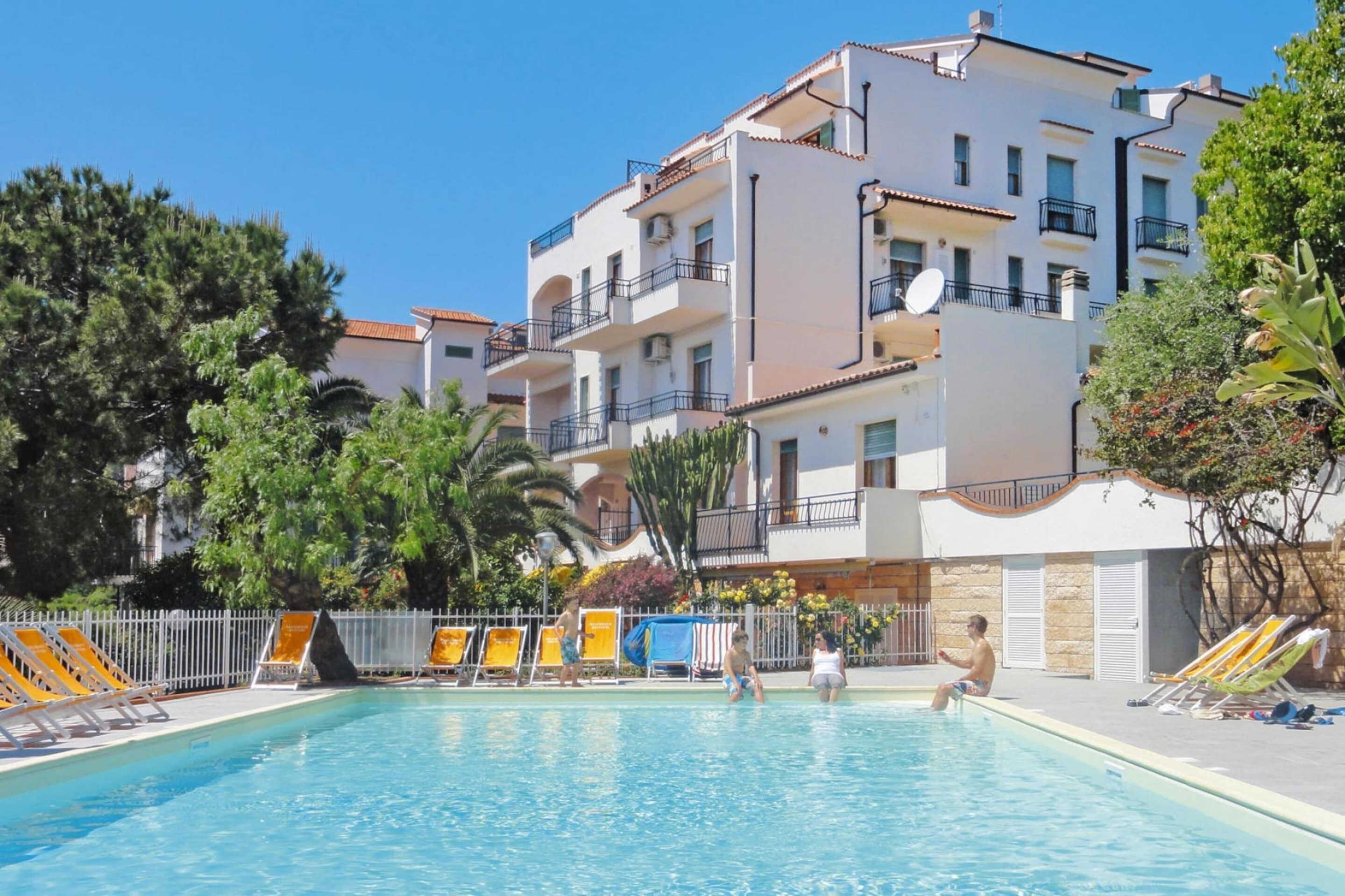 A swimming pool area with lounge chairs and a building with balconies.