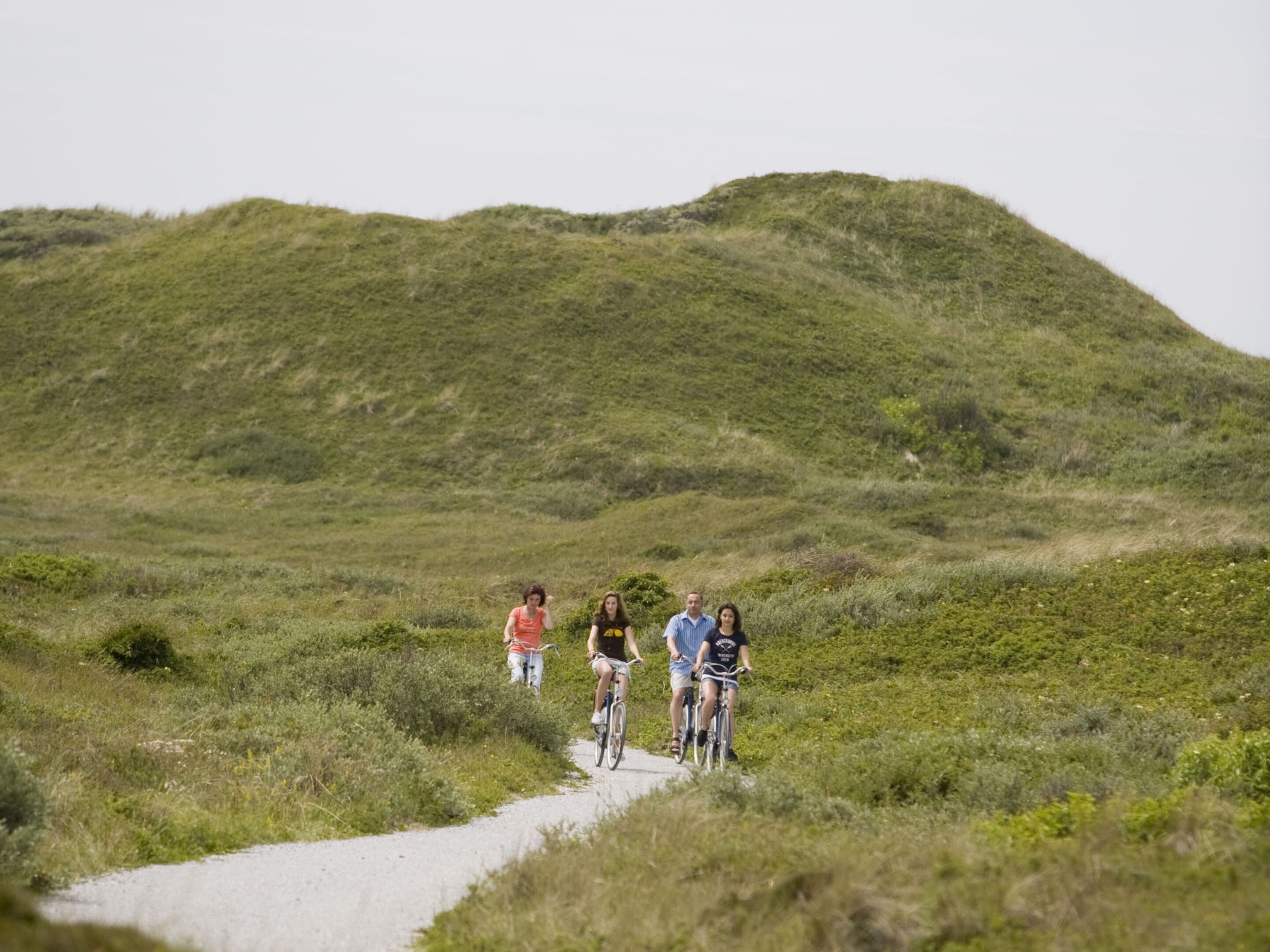 Eine Gruppe von Menschen fährt auf einem Schotterweg, umgeben von sanften Hügeln.