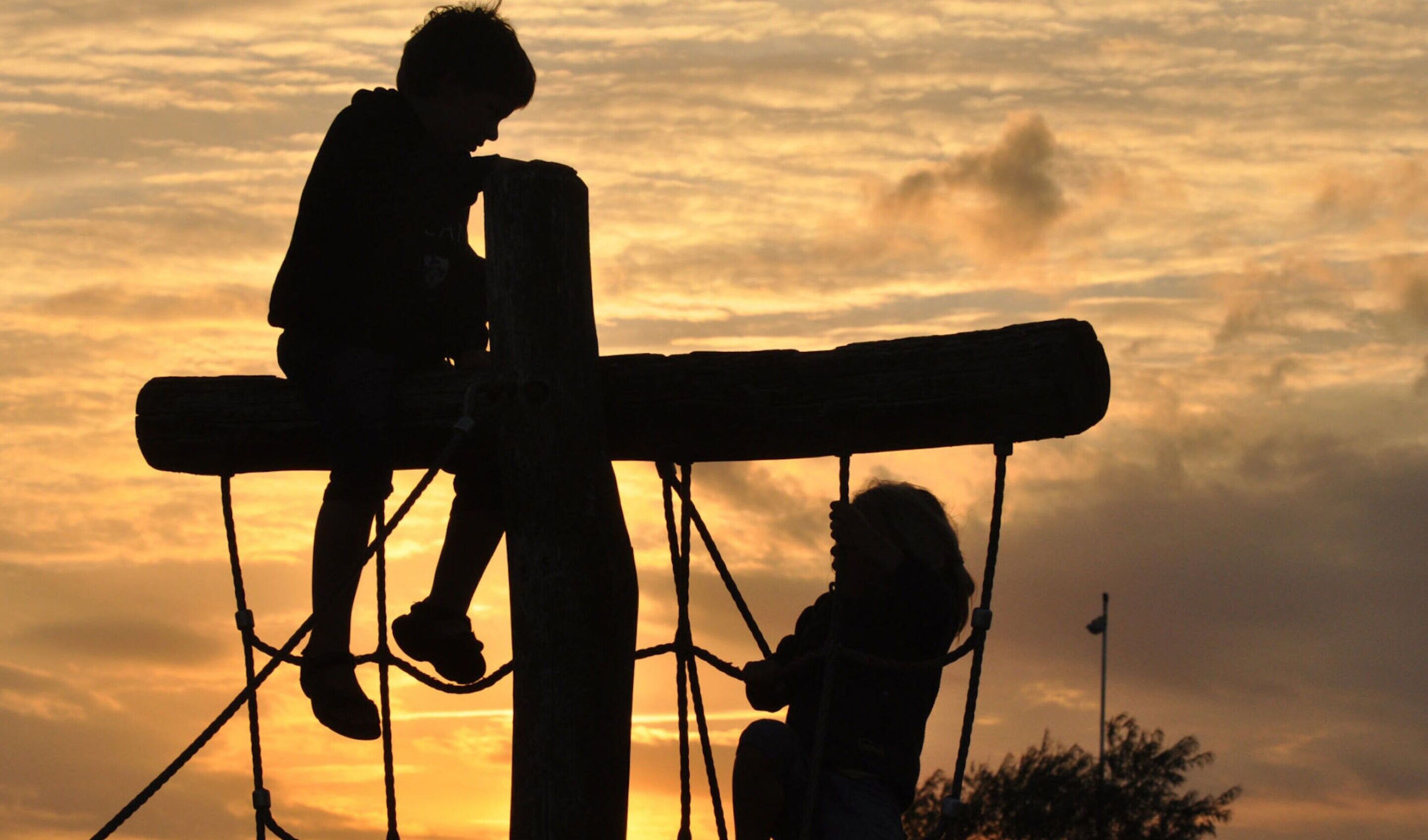 Dos siluetas de personas sobre una estructura contra un cielo al atardecer.