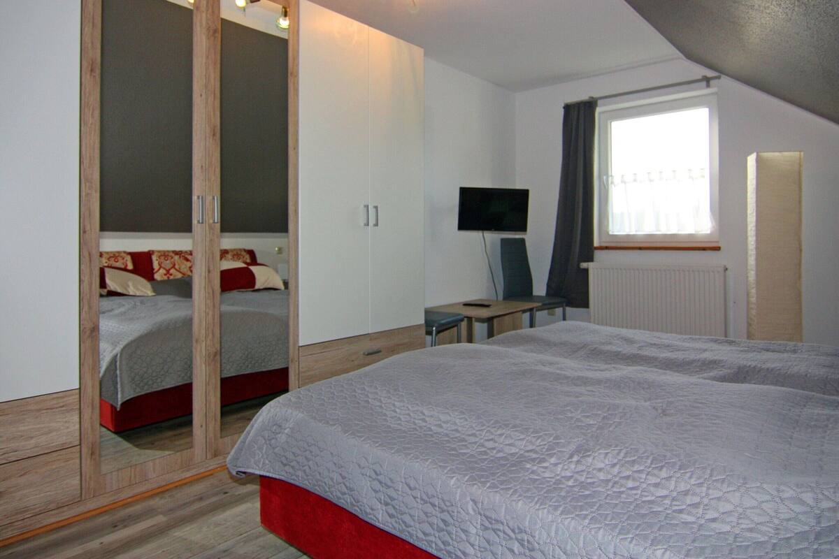A bedroom with a bed, a desk, a TV, and a wardrobe.