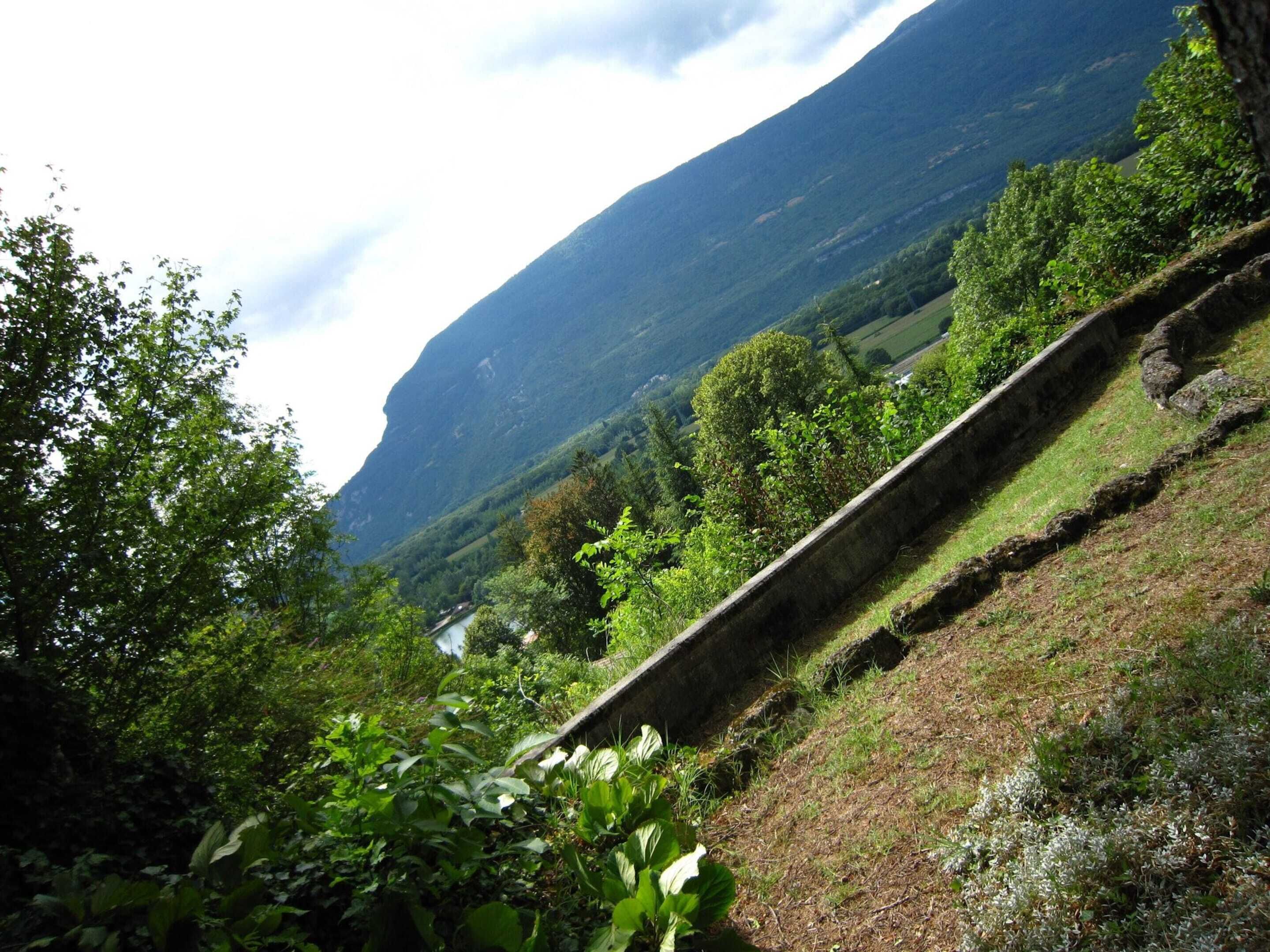 A mountainous landscape with a stone retaining wall and lush greenery.