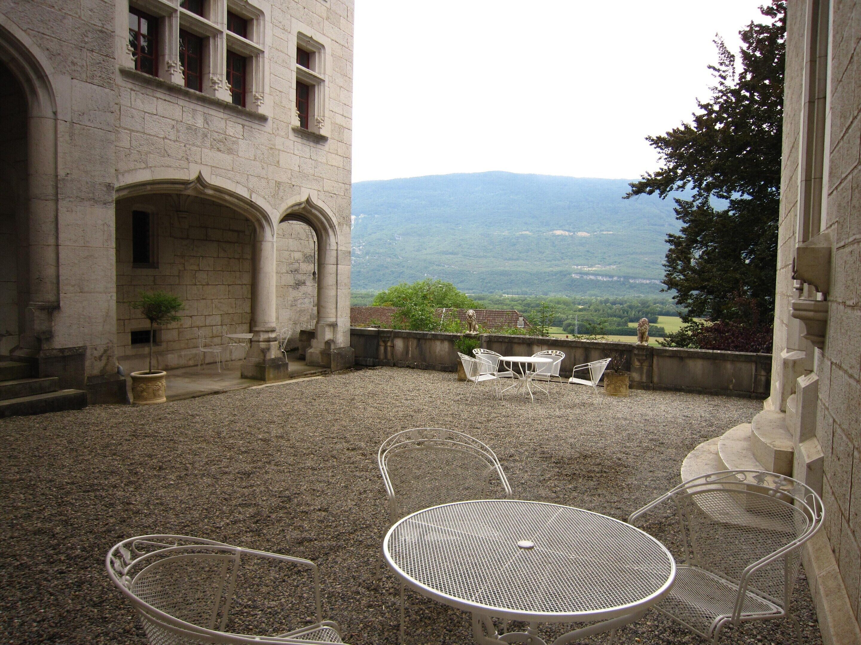 A courtyard with a stone building, a small tree, and a view of distant hills.