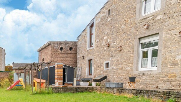 Un edificio de piedra con una sección de ladrillo, una estructura de madera para juegos y un cielo despejado.