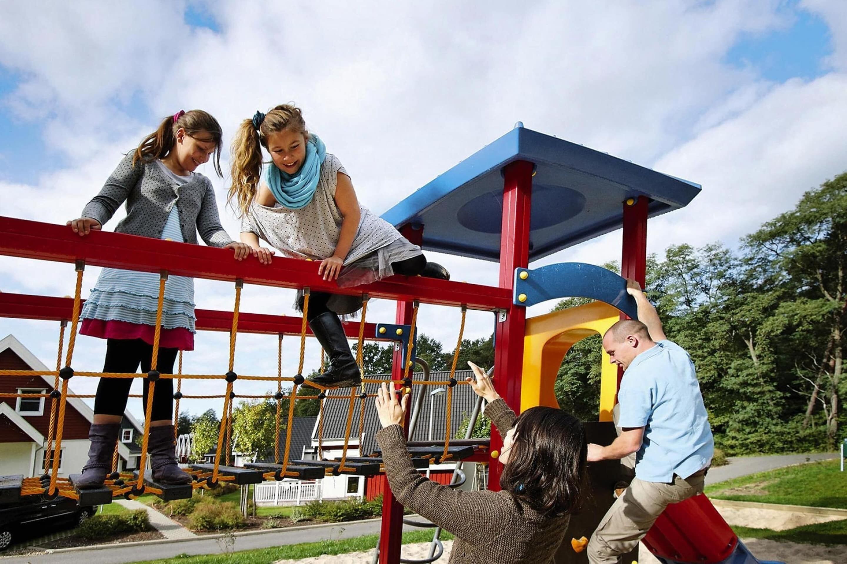 A playground with a red and yellow play structure, including a rope bridge and slides.