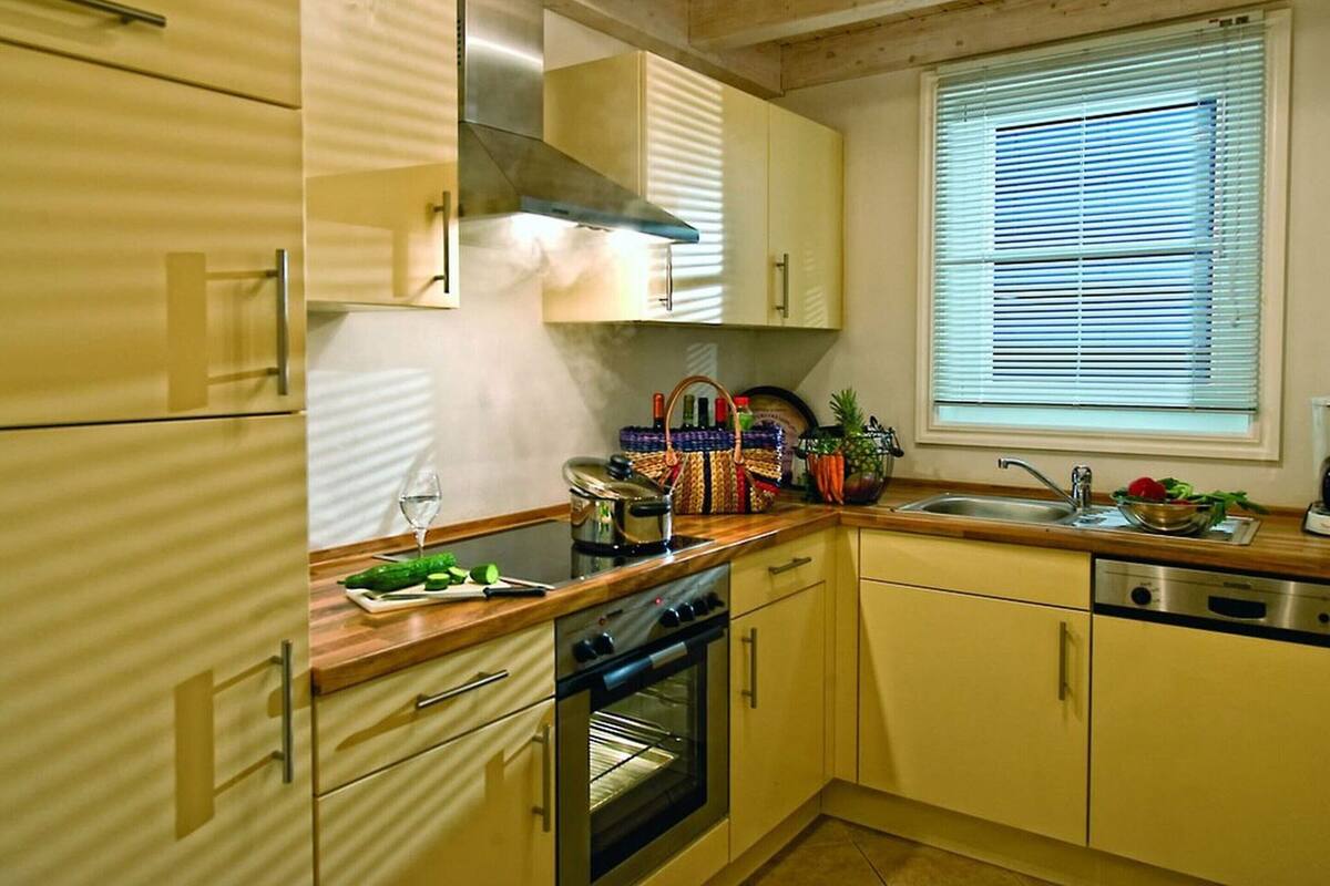 A kitchen with wooden cabinets, a stove, an oven, a sink, and a window with blinds.