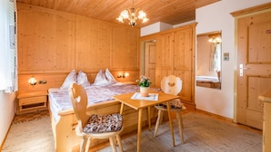 Ein Zimmer mit Holzwänden, einem Bett, zwei Stühlen, einem Tisch und einer Kristallleuchter.