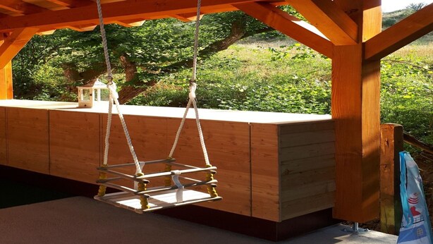 Une terrasse en bois avec une balançoire, une lanterne et une vue sur la verdure.