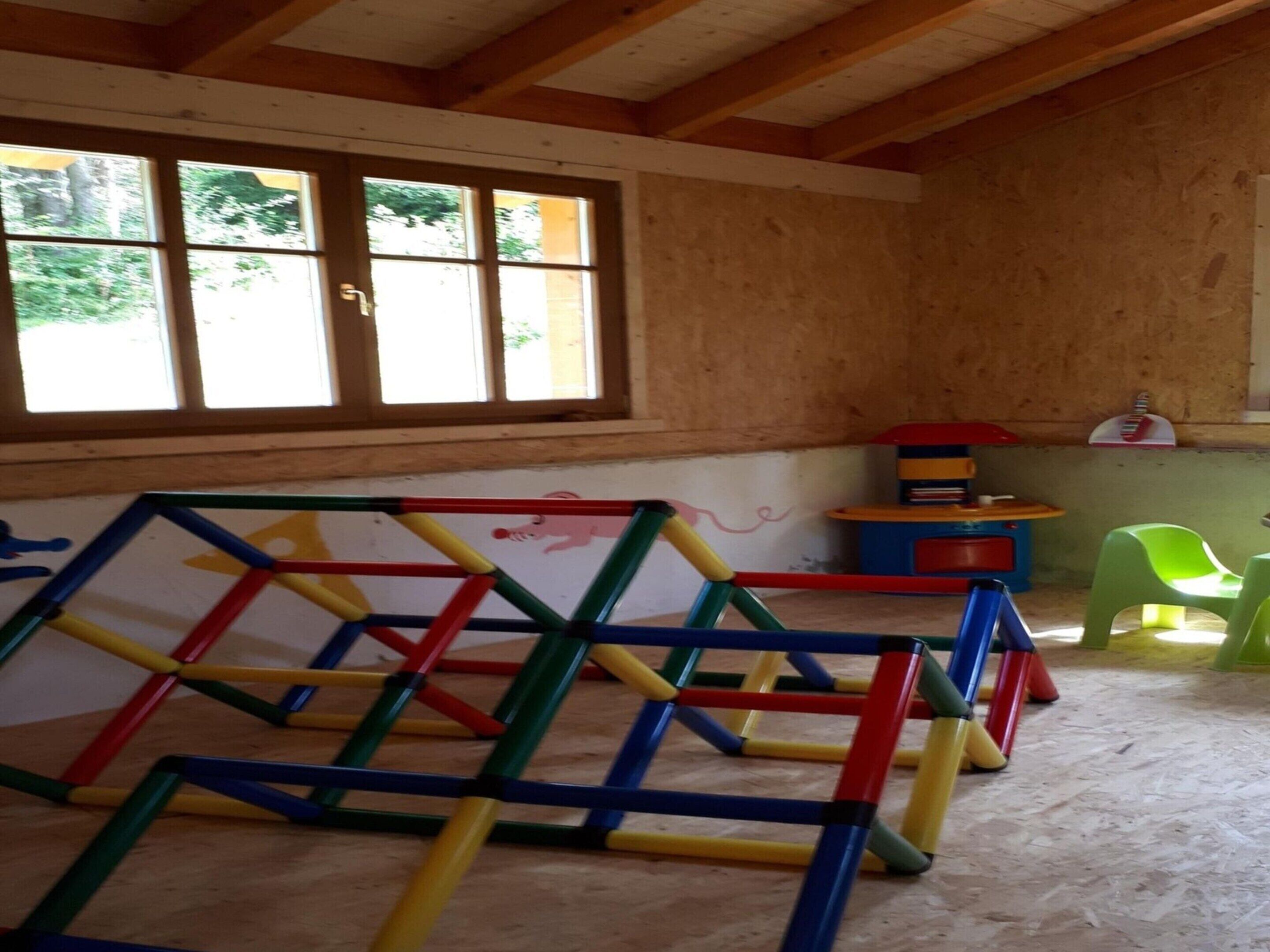 A room with a wooden ceiling and a window with four panes. There is a colorful play structure in the center and a small table with a toy on it.