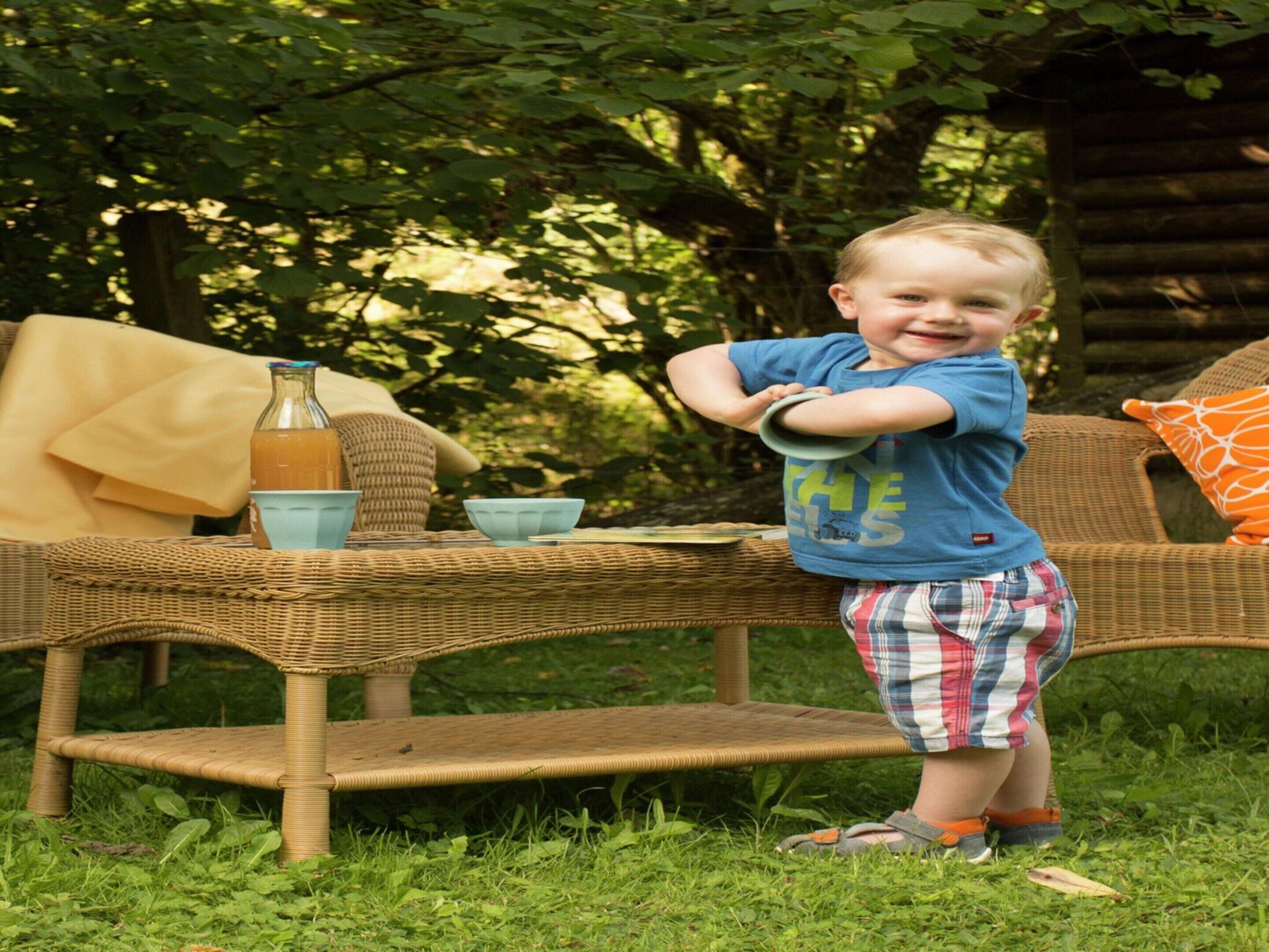 A child standing by a wicker table with a bottle and bowls.