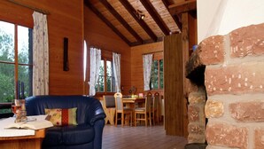 L’intérieur chaleureux d’un chalet avec un canapé en cuir bleu, un coin repas avec des chaises en bois, un sol carrelé et une cheminée en pierre.