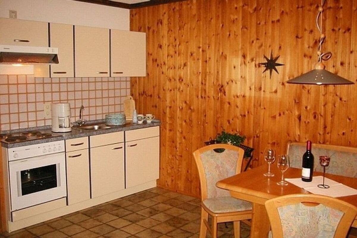 A kitchen with wooden paneling, a dining table with chairs, and a hanging light fixture.