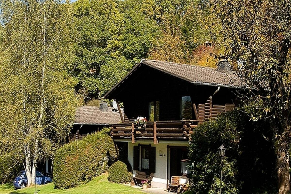 A log cabin with a balcony, surrounded by lush greenery and a clear sky.