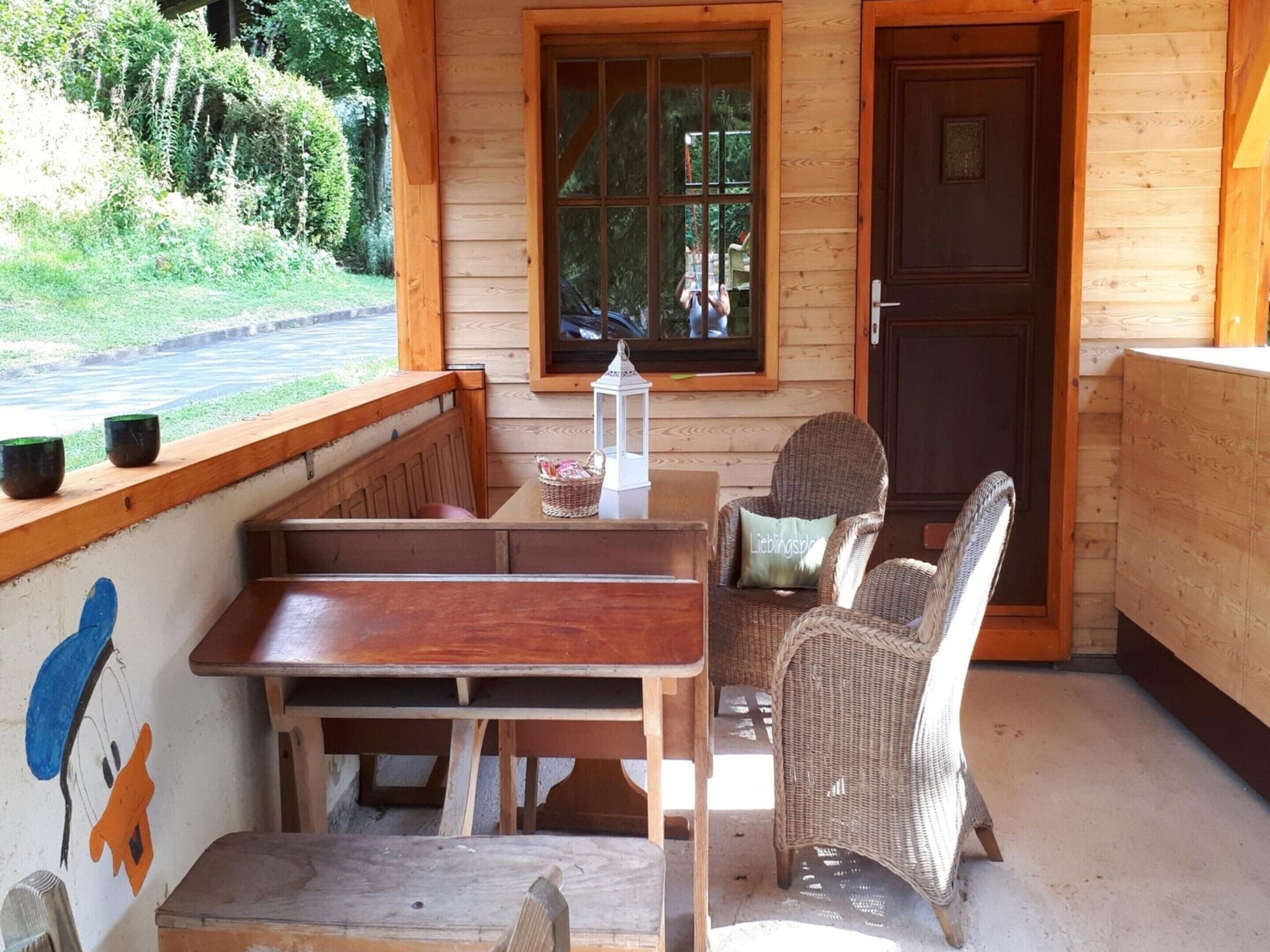 A wooden cabin with a porch, a wooden bench, wicker chairs, and a table.