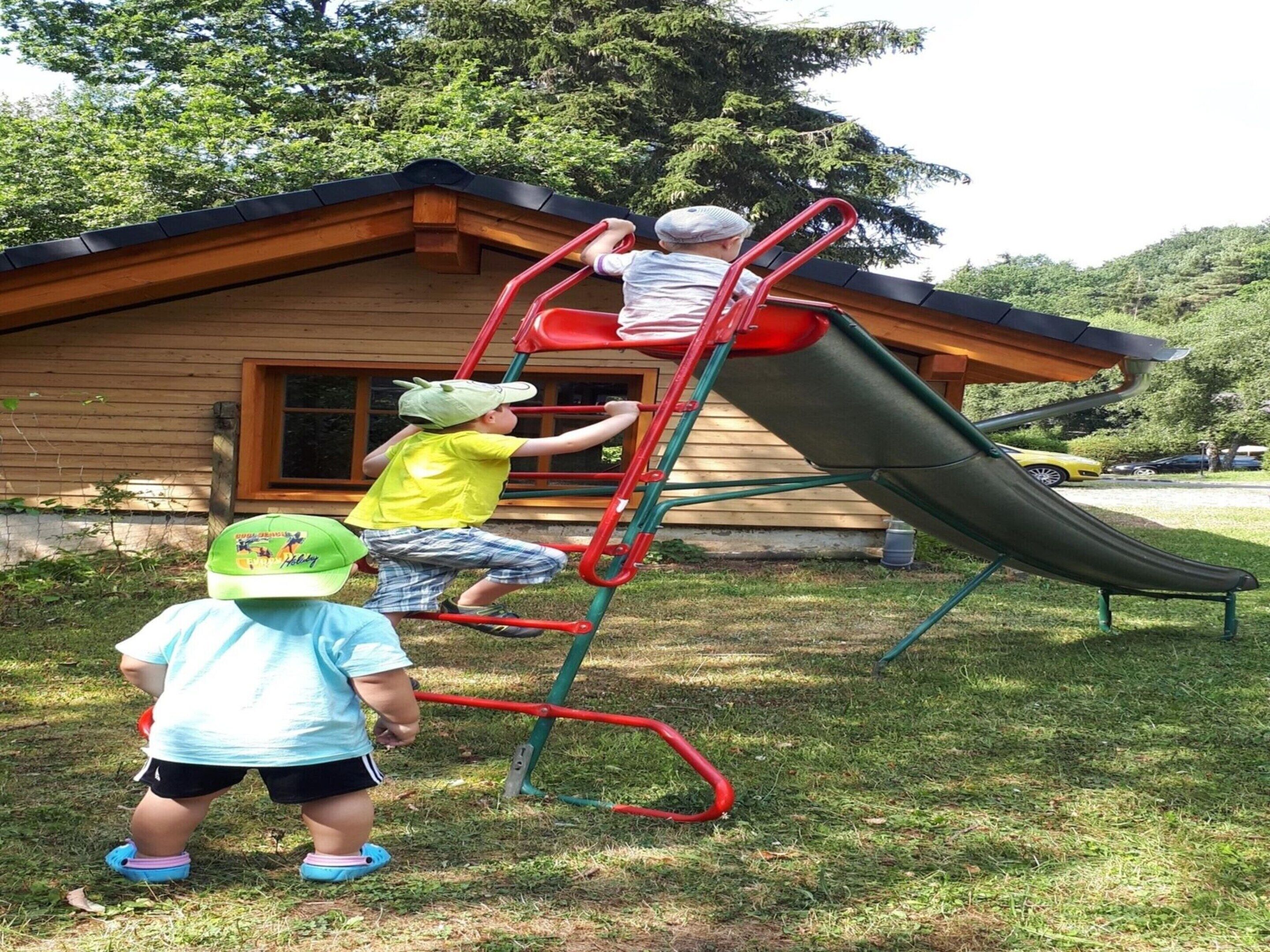 A wooden cabin with a red metal slide and climbing structure.