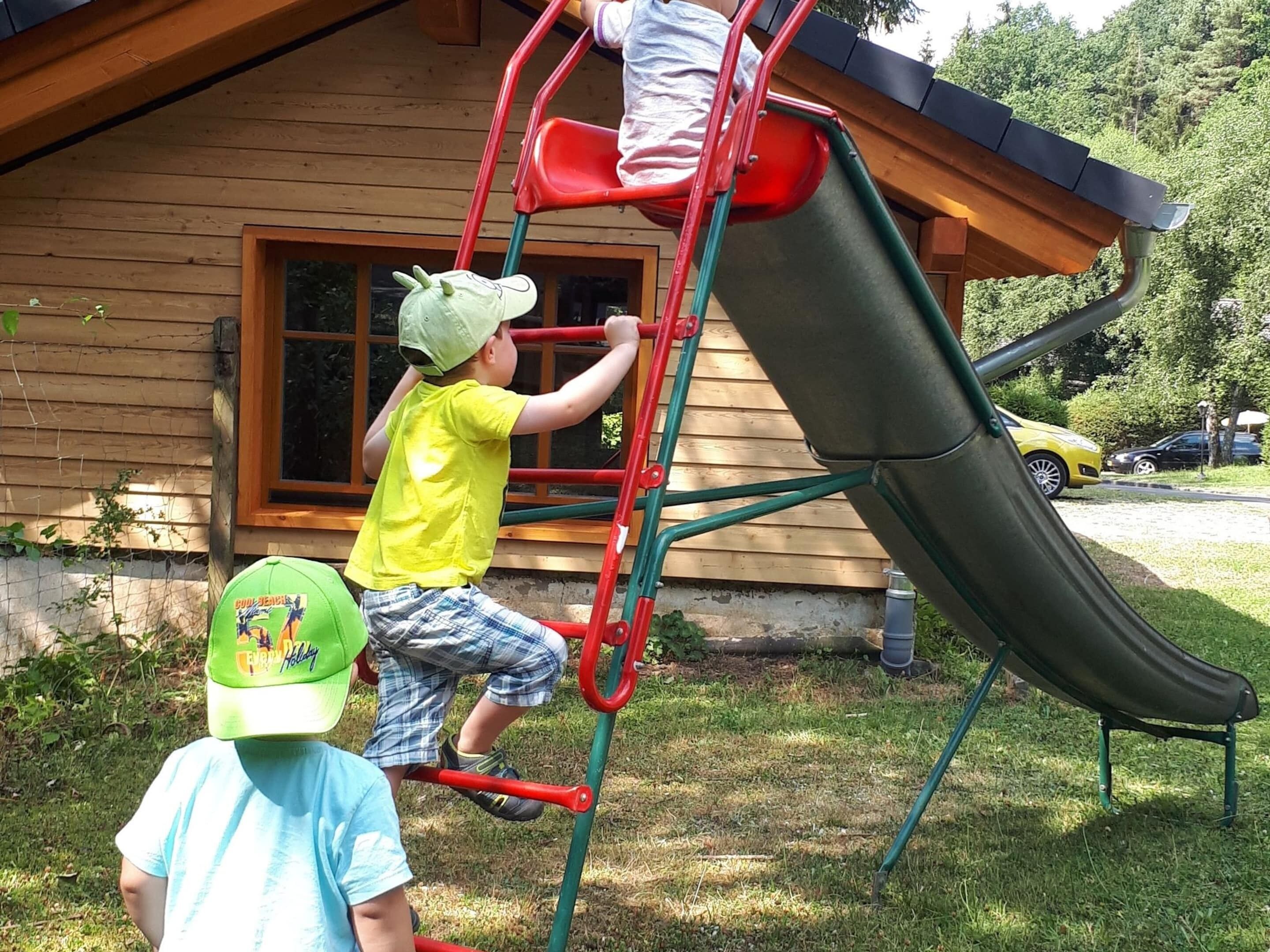 A playground with a slide and climbing structures in front of a wooden building.