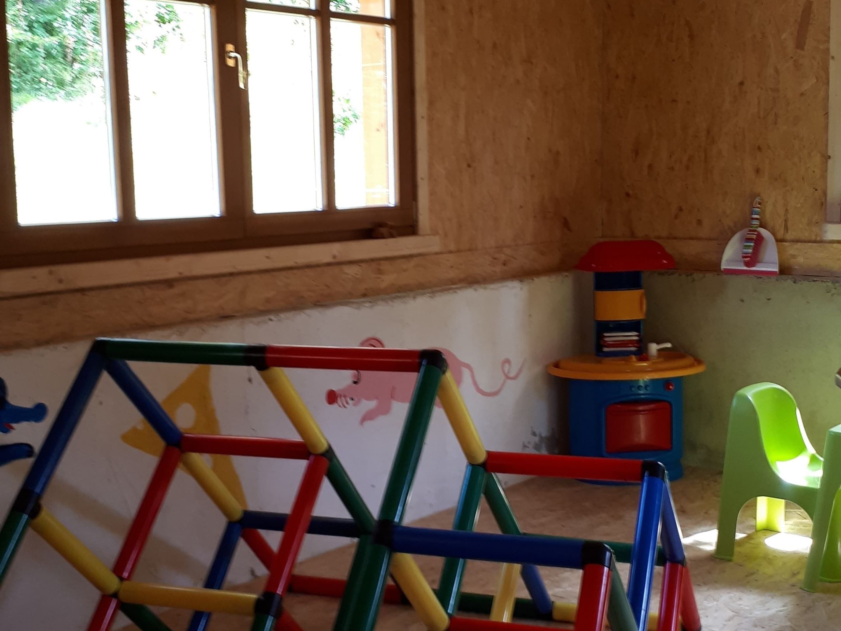 A room with a window, a colorful play structure, a toy kitchen set, and a green chair.