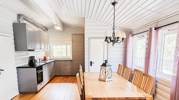 A spacious kitchen with wooden cabinets, a dining table with chairs, and a chandelier. - 8 Person Holiday Home in Aseral (Aseral)