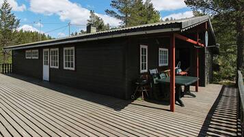 A wooden cabin with a covered porch, a small outdoor seating area, and a satellite dish.