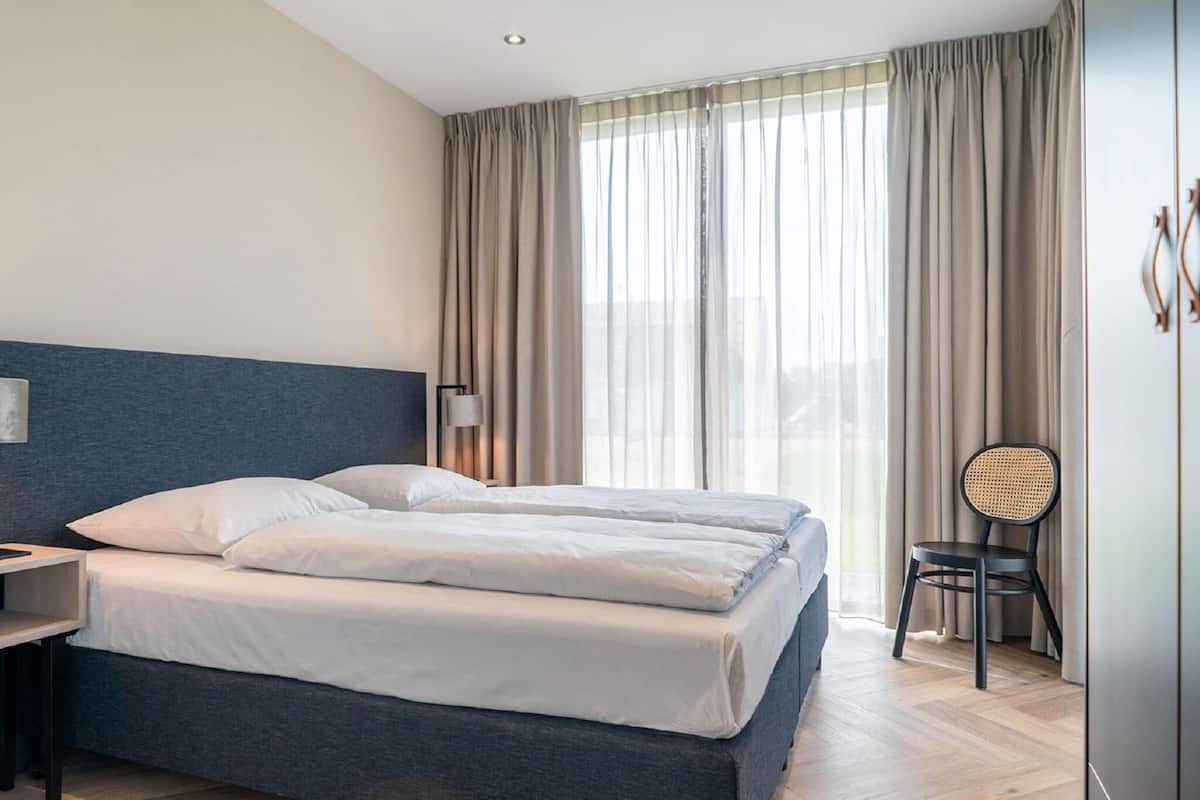 Hotellihuone, jossa on sänky, työpöytä, tuoli ja suuri ikkuna, jossa on verhot.