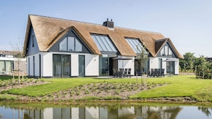A modern house with a thatched roof, large windows, and a pond in the front yard. - Semi-detached, Luxury Villa With 3 Bathrooms, sea at 400 m (De Koog)