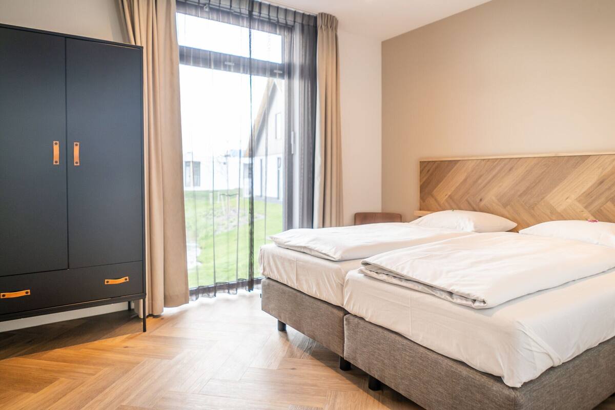 Hotellihuone, jossa on kaksi sänkyä, vaatekaappi ja suuri ikkuna, jossa on verhot.