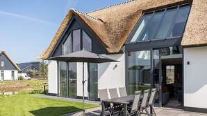 A modern house with a thatched roof, large windows, and a patio with a table and chairs. - Semi-detached, Luxury Villa With 3 Bathrooms, sea at 400 m (De Koog)