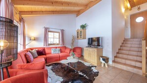 A cozy living room with a red sofa, a wooden cabinet, a television, and a staircase. - Luxurious Chalet With Sauna in Konigsleiten (Wald im Pinzgau)