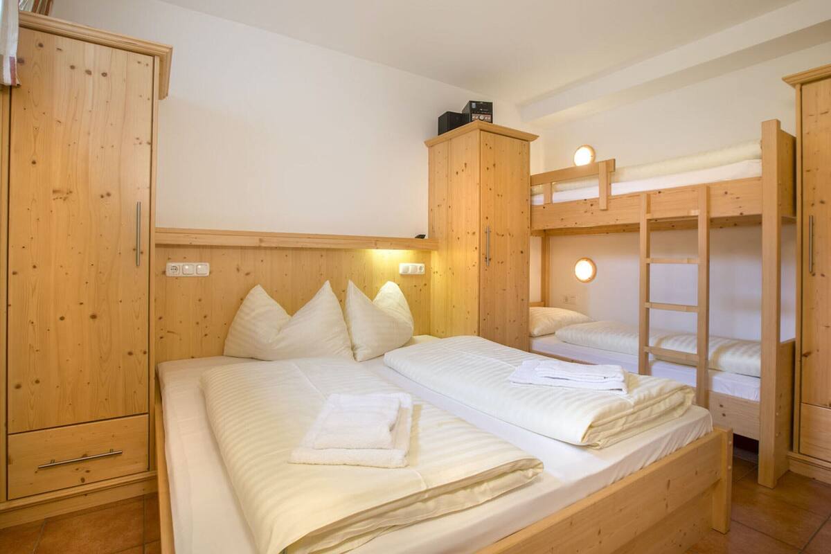 A wooden bunk bed room with a single bed and a bunk bed. There are wooden cabinets and a small shelf with a radio.