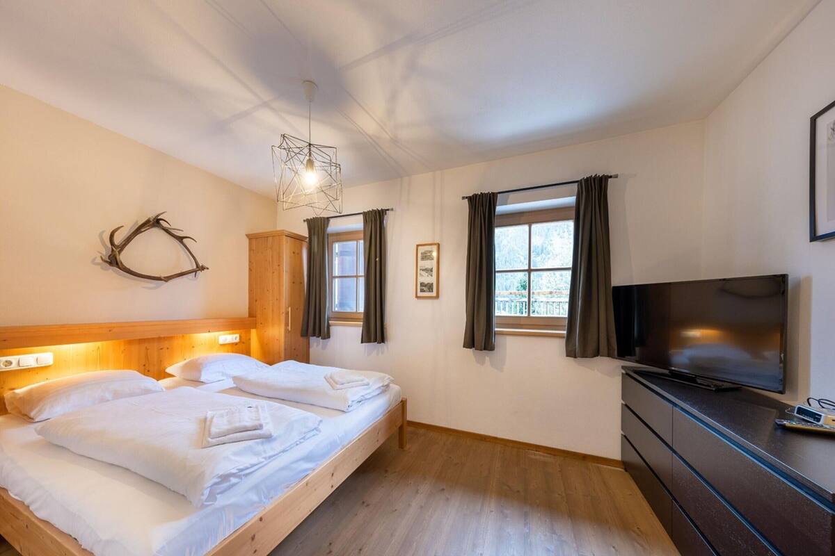 A bedroom with a wooden bed, a TV, and a window with curtains.