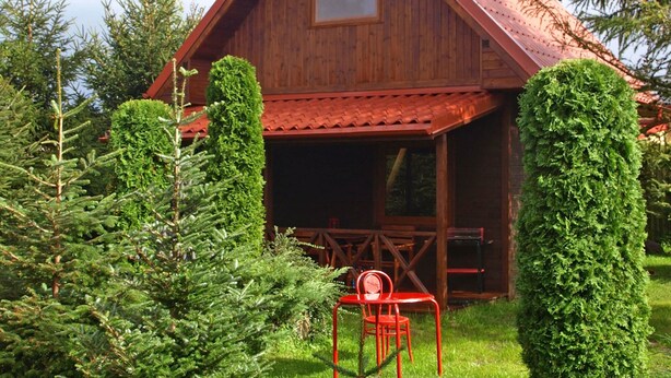 A wooden cabin with a pitched roof, a small window, and a covered porch. - Authentic Holiday Home in Kopalino With Fireplace (Choczewo)