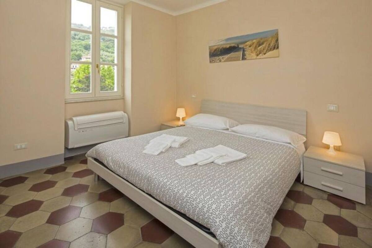 A bedroom with a bed, two bedside tables, a window, and a radiator.