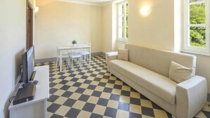 A room with a checkered floor, a white sofa, a small table with chairs, and a TV on a stand. - Apartment in Lerici With Garden (Lerici)
