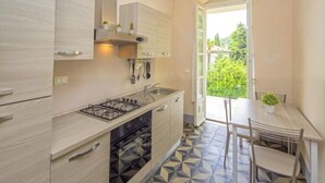 A modern kitchen with a gas stove, oven, and a dining area with a table and chairs. - Apartment in Lerici With Garden (Lerici)