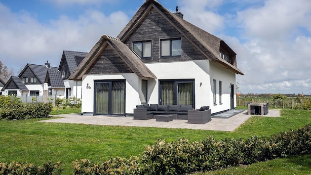 A modern two-story house with a large patio, a thatched roof, and a well-maintained lawn. - Nice Bungalow With Dishwasher in a Holiday Park 1.2 km. From the sea on Texel (De Koog)