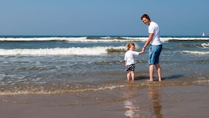 A beach scene with a man and a child holding hands, standing in shallow water. - Nice Bungalow With Dishwasher in a Holiday Park 1.2 km. From the sea on Texel (De Koog)