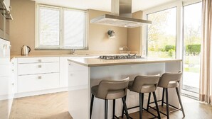 A modern kitchen with a large island, bar stools, a gas stove, and a stainless steel range hood. - Nice Bungalow With Dishwasher in a Holiday Park 1.2 km. From the sea on Texel (De Koog)