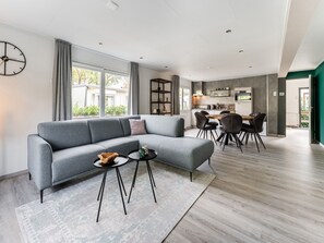 Een moderne woonkamer met een grijze hoekbank, een salontafel en een eethoek met een houten tafel en stoelen.