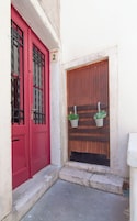Una puerta roja con un cartel con el número '2', una puerta de madera con dos macetas y un escalón pequeño que lleva a la puerta.