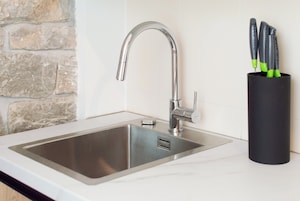 A modern kitchen sink with a sleek faucet, a black utensil holder, and a stone wall backsplash.