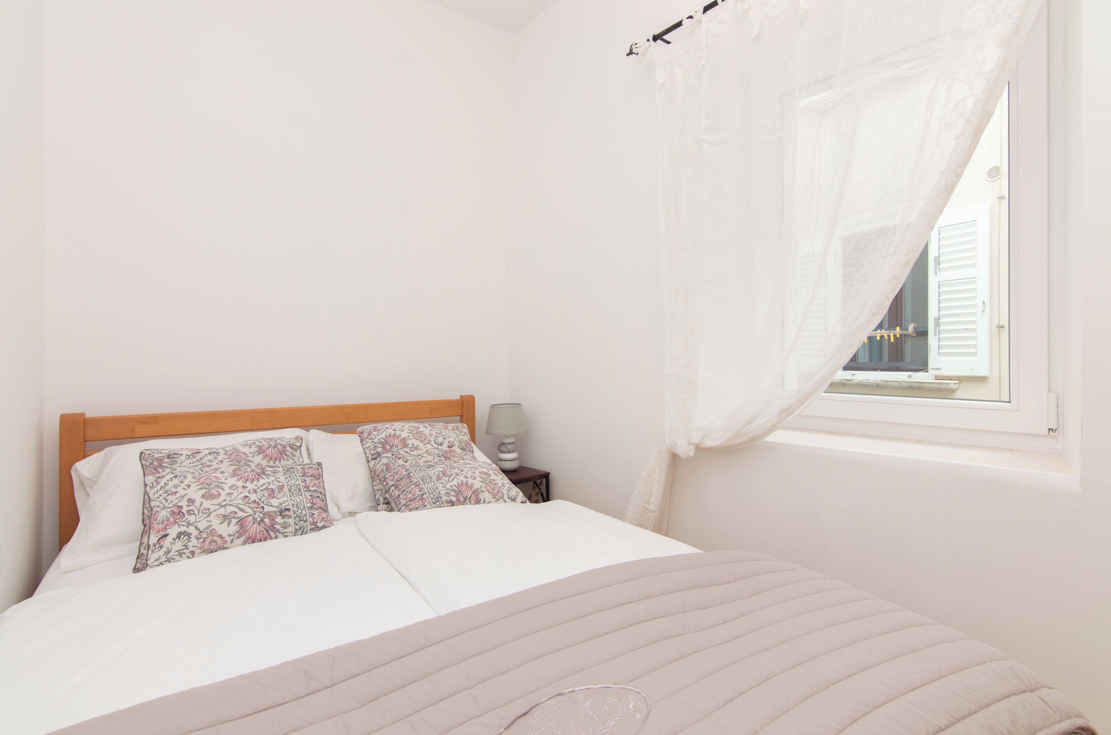 A bedroom with a bed, a nightstand, a lamp, and a window with a curtain.