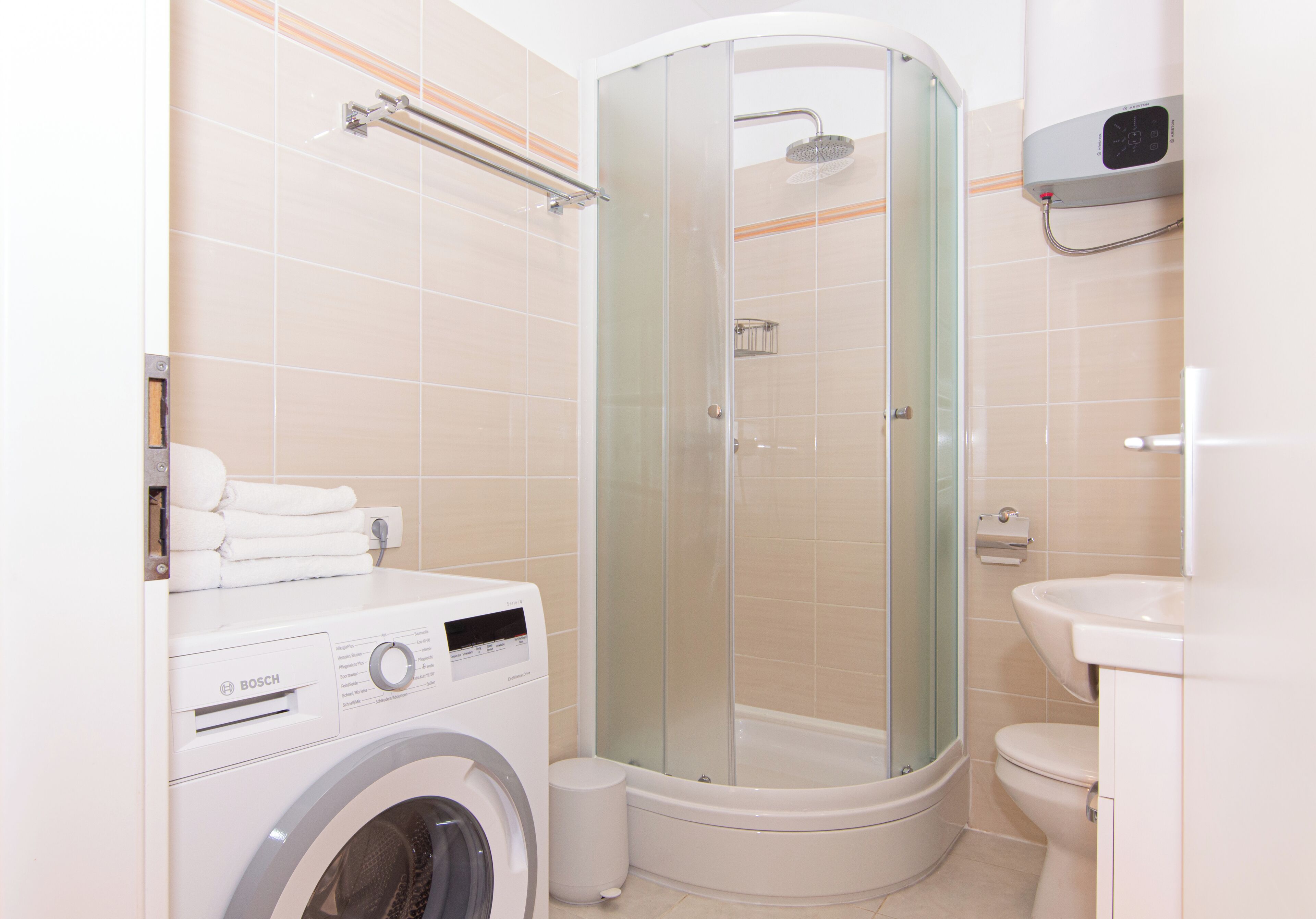 Un baño moderno con ducha de vidrio, lavadora Bosch, inodoro y lavamanos.