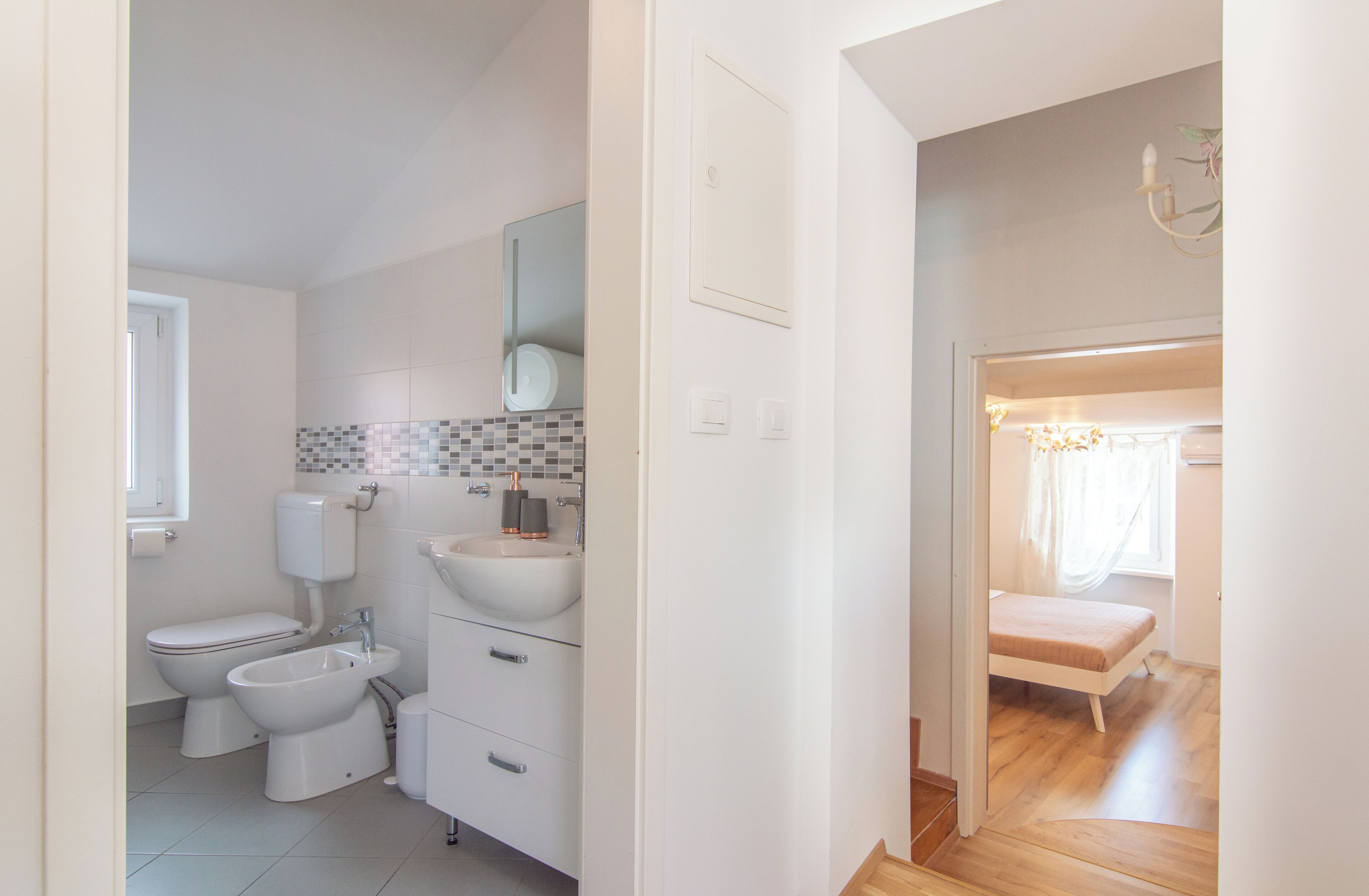 A modern bathroom with a toilet, bidet, sink, and mirror.