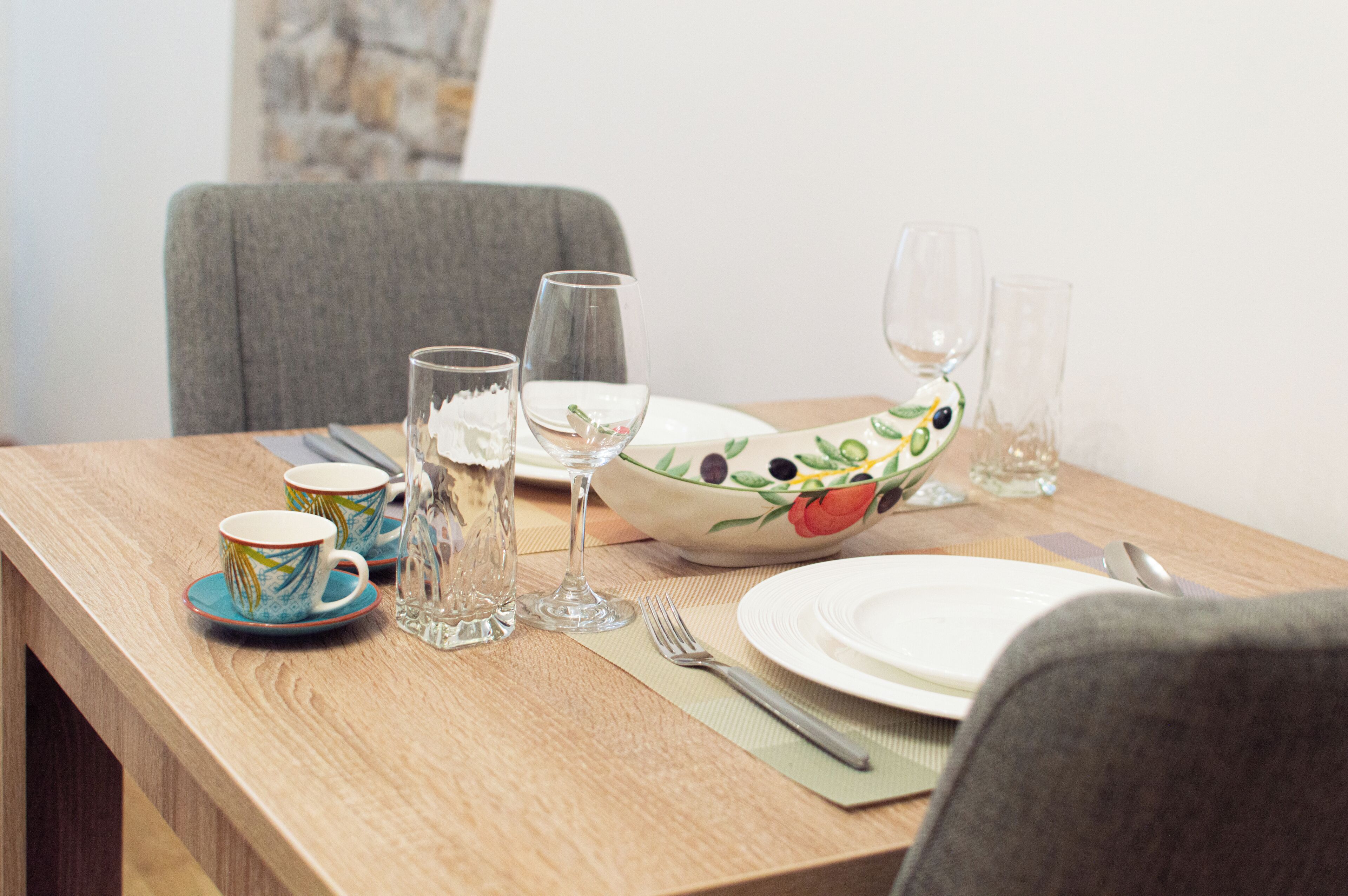 Une table à manger dressée avec un saladier, des assiettes, des tasses, des verres et des couverts.