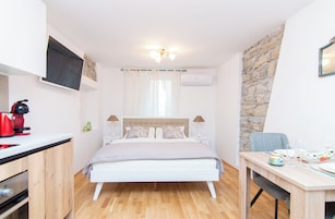 A modern bedroom with a bed, bedside tables, a desk, and a stone wall.