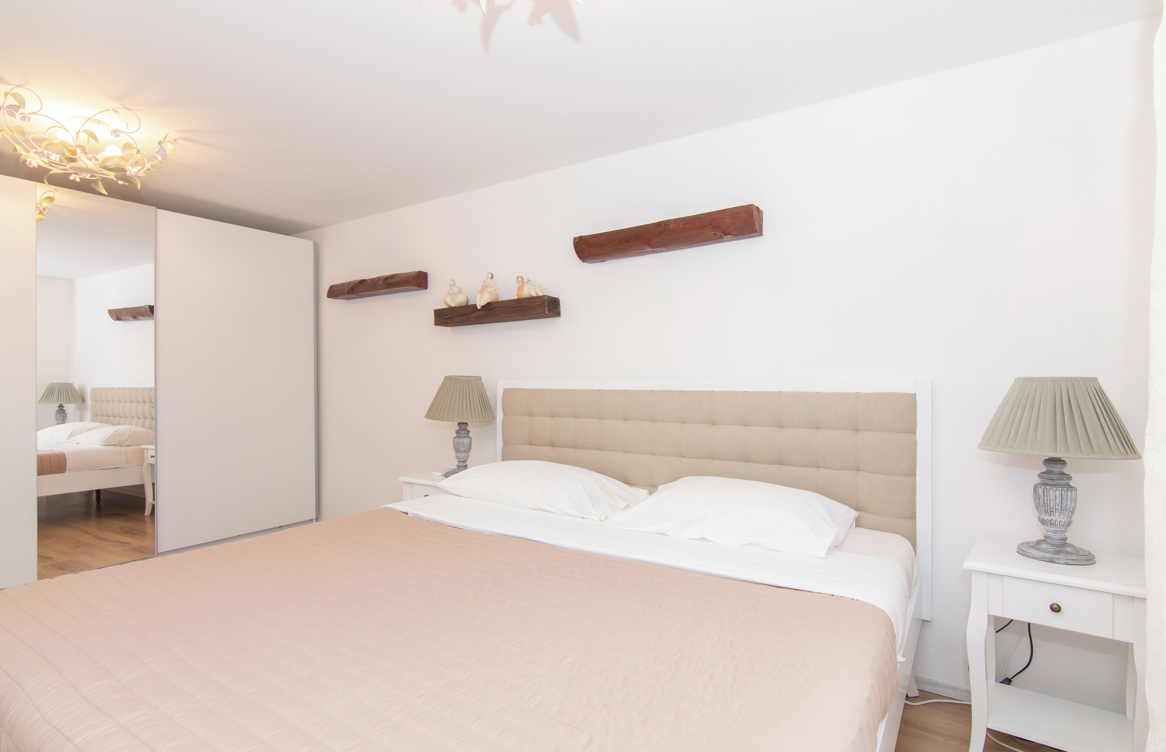 A bedroom with a large bed, two bedside tables, a mirror, and a ceiling light fixture.