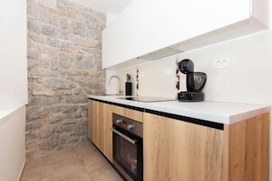 A modern kitchen with a stone wall, wooden cabinets, a built-in oven, and a coffee machine.