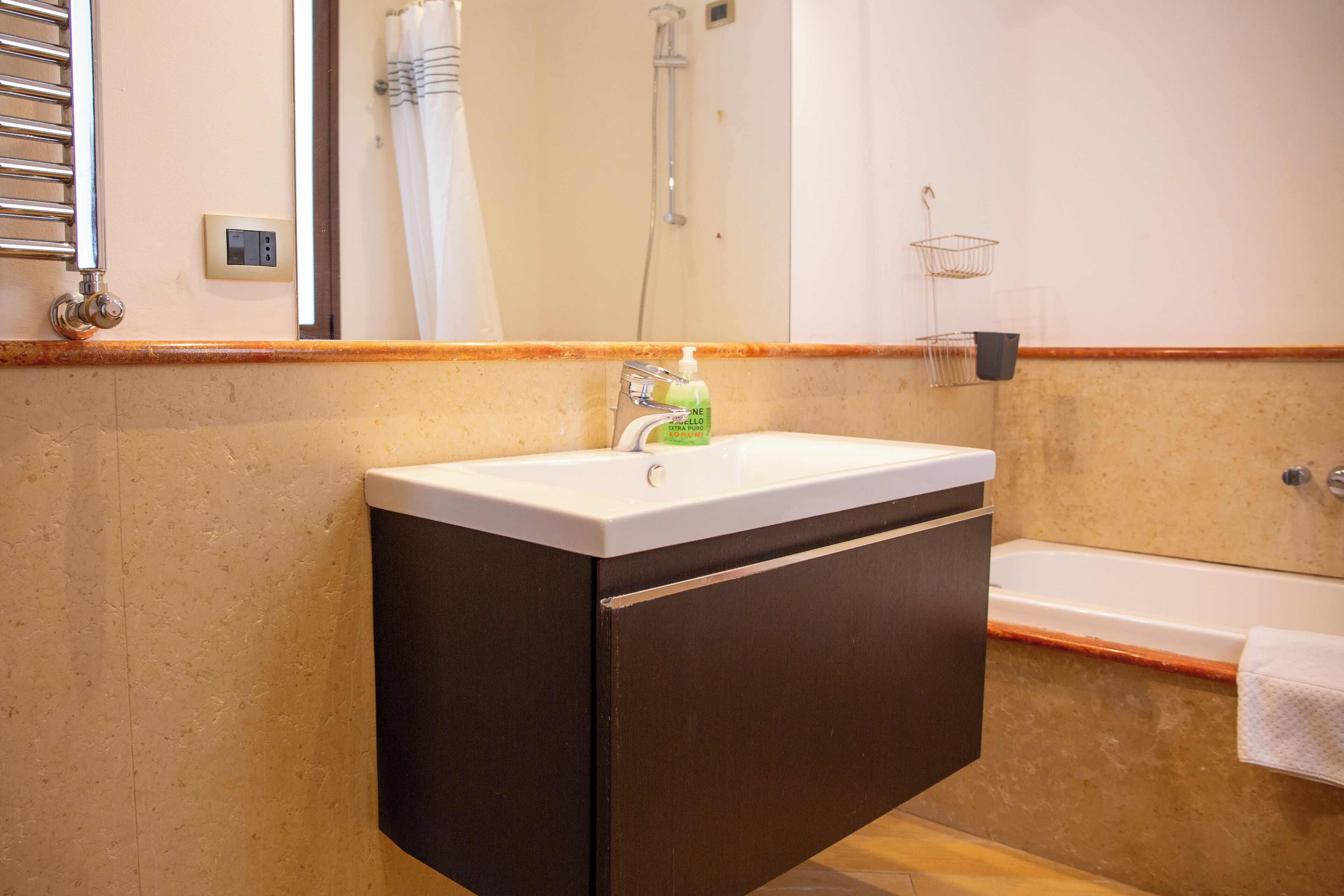 Een badkamer met een wit wastafelmeubel, donkere kastjes, een douche en een handdoekrek.