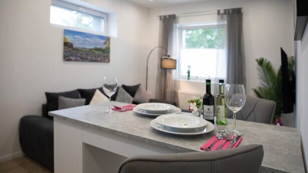 A modern dining area with a central island, two chairs, a sofa, and a painting on the wall. - HANNIBAL - Design Apartment Lavendel 4 (Wolfsburg)